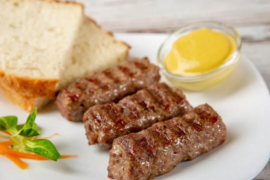 Mititei delicioși serviți cu muștar și pâine proaspătă.