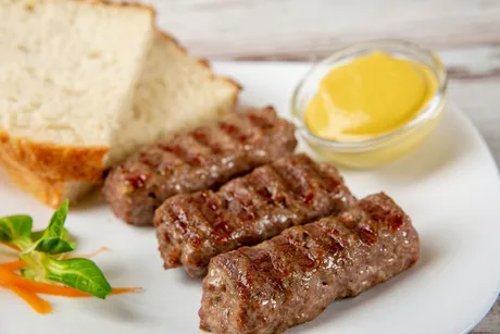 Mititei delicioși serviți cu muștar și pâine proaspătă.