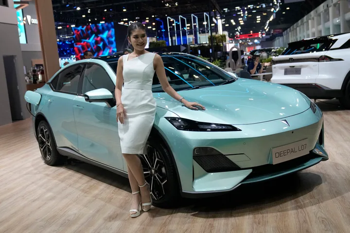 O femeie stă lângă un automobil electric pe un fundal de expoziție auto.