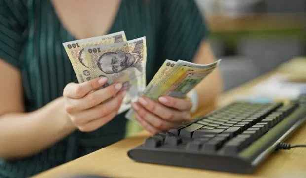 O persoană numără bancnote pe un birou, evidențiind aspecte financiare.