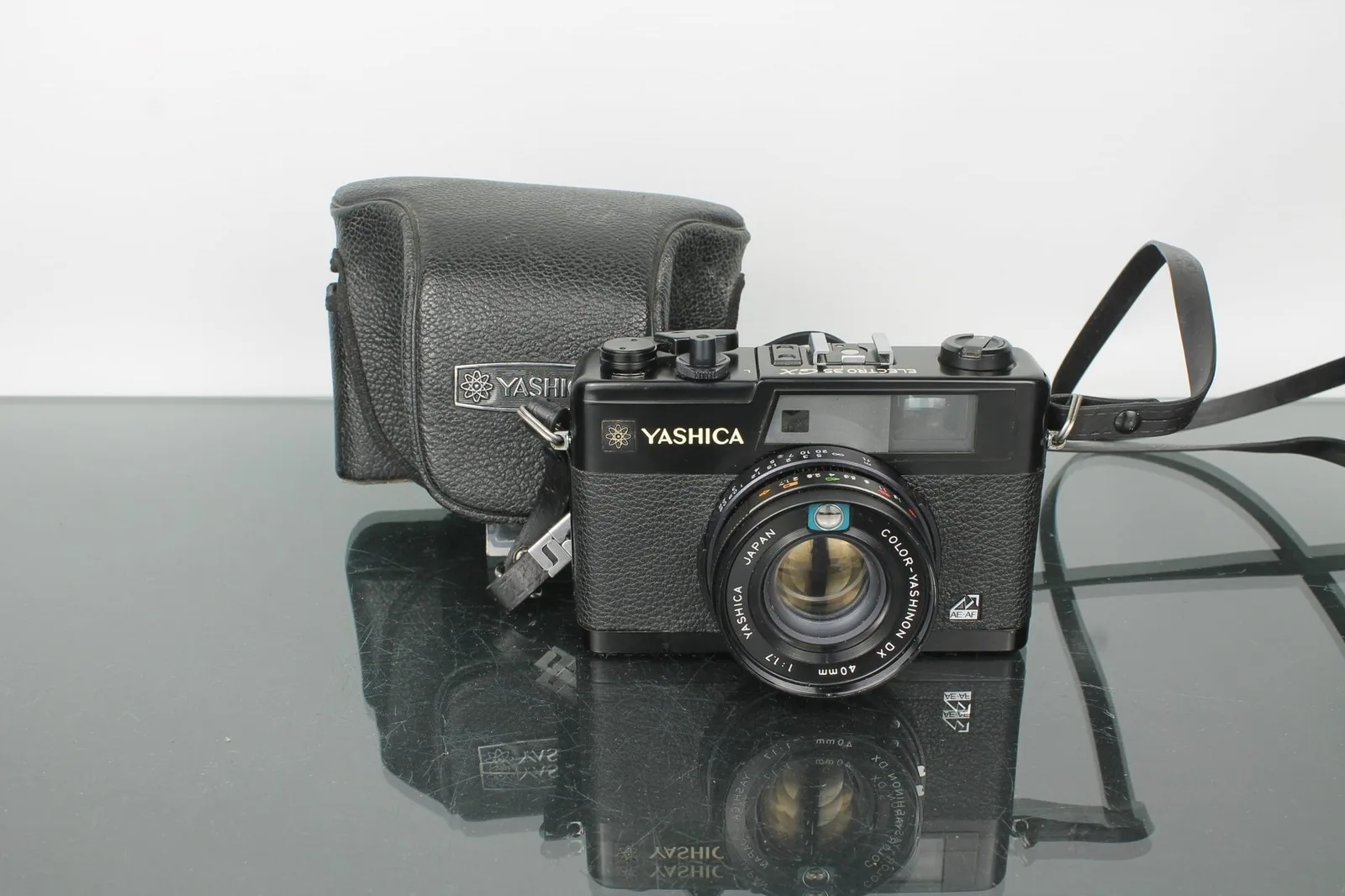 Cameră Yashica pe un fundal negru, cu husă de protecție.