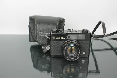 Cameră Yashica pe un fundal negru, cu husă de protecție.