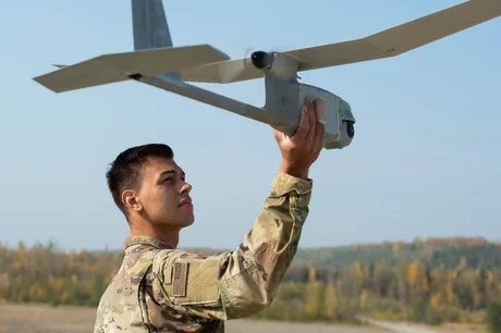 Un soldat pregătește o dronă pentru zbor într-un peisaj militar.