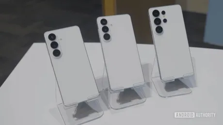 Trei telefoane Galaxy S27 aliniate pe un suport transparent, cu spatele alb.