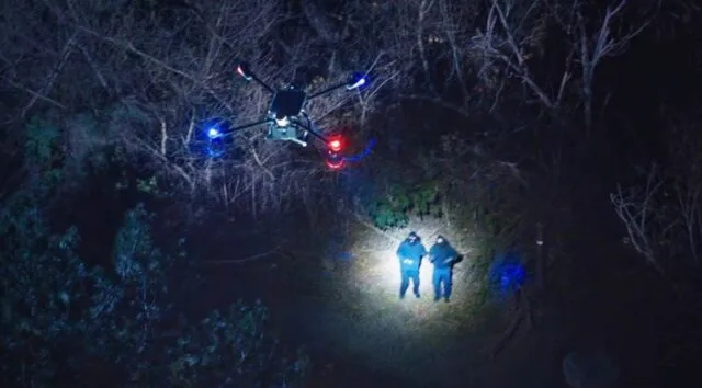 Dronă de poliție în acțiune, iluminând zona cu lumini albastre și roșii.