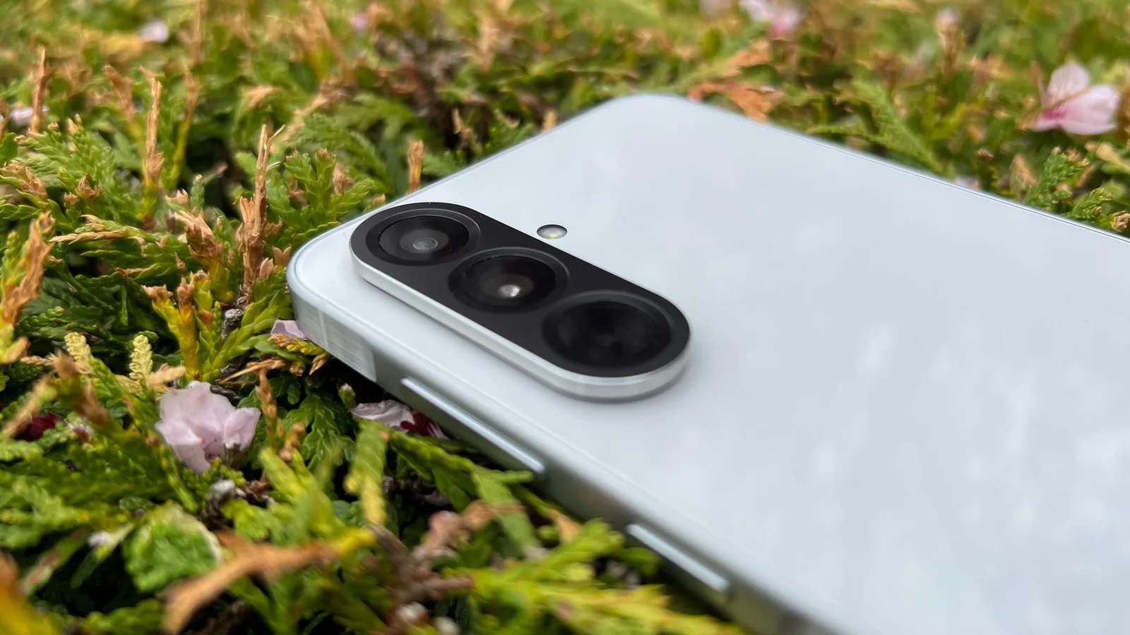 Detaliu al camerei unui smartphone pe un fundal natural.