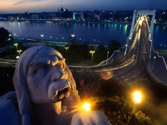 Vedere nocturnă a unui pod din Budapesta, cu sculpturi și lumini strălucitoare.