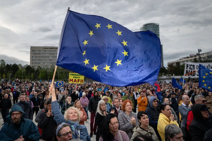 Oamenii protestează cu steagul Uniunii Europene în fundal.