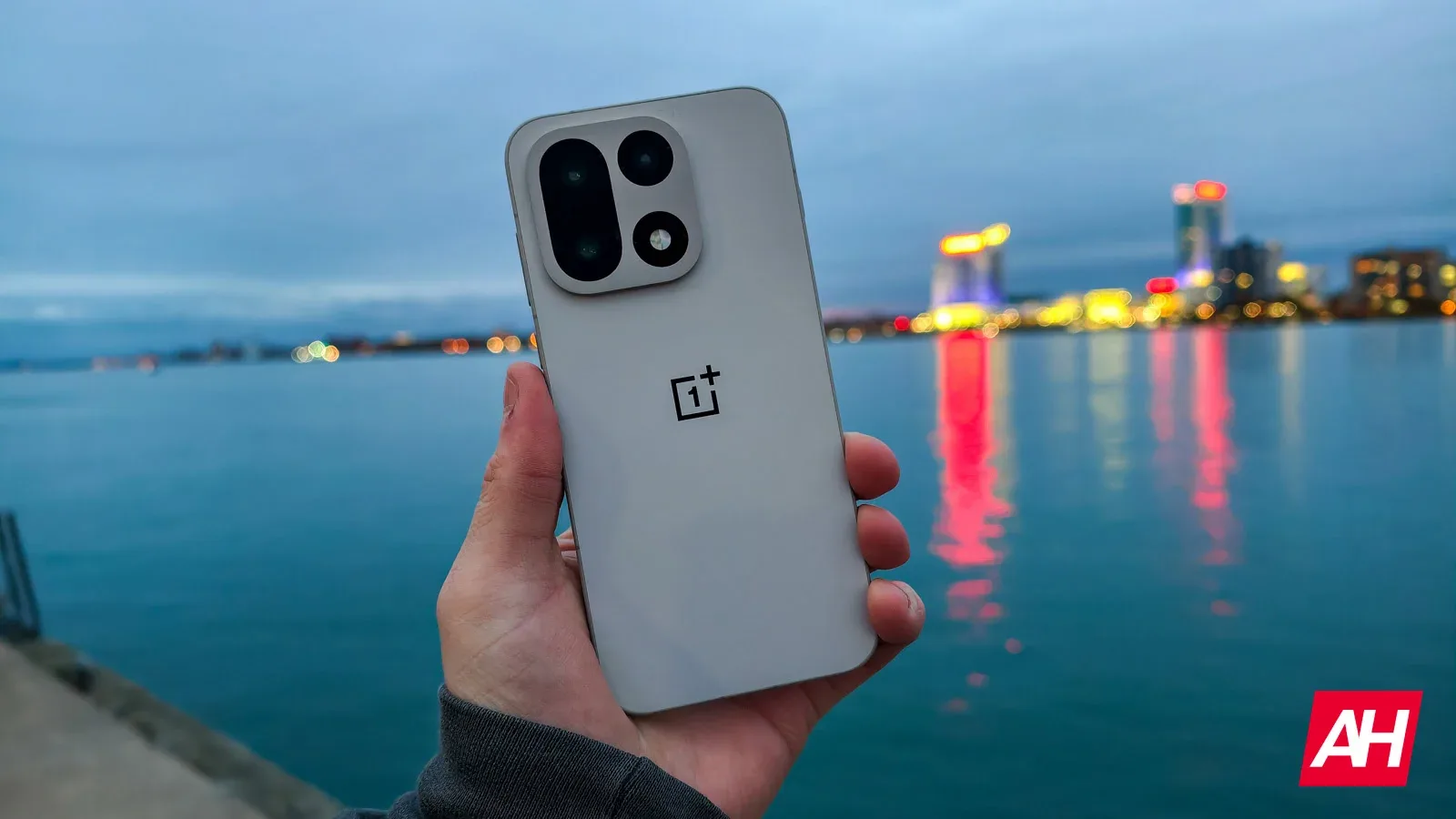 Un smartphone OnePlus pe malul apei, cu orașul iluminat în fundal.