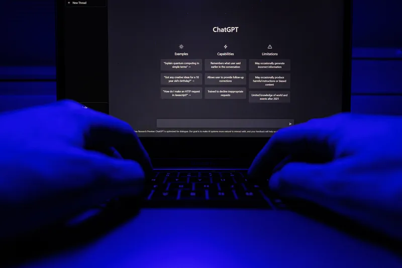 Ecran de laptop cu interfața ChatGPT în lumina albastră, mâini pe tastatură.