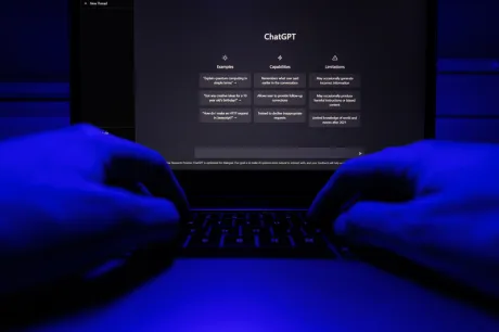 Ecran de laptop cu interfața ChatGPT în lumina albastră, mâini pe tastatură.