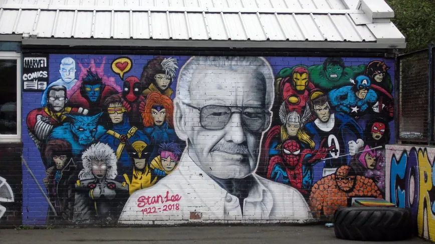 Graffiti cu Stan Lee și personaje Marvel pe un zid colorat.