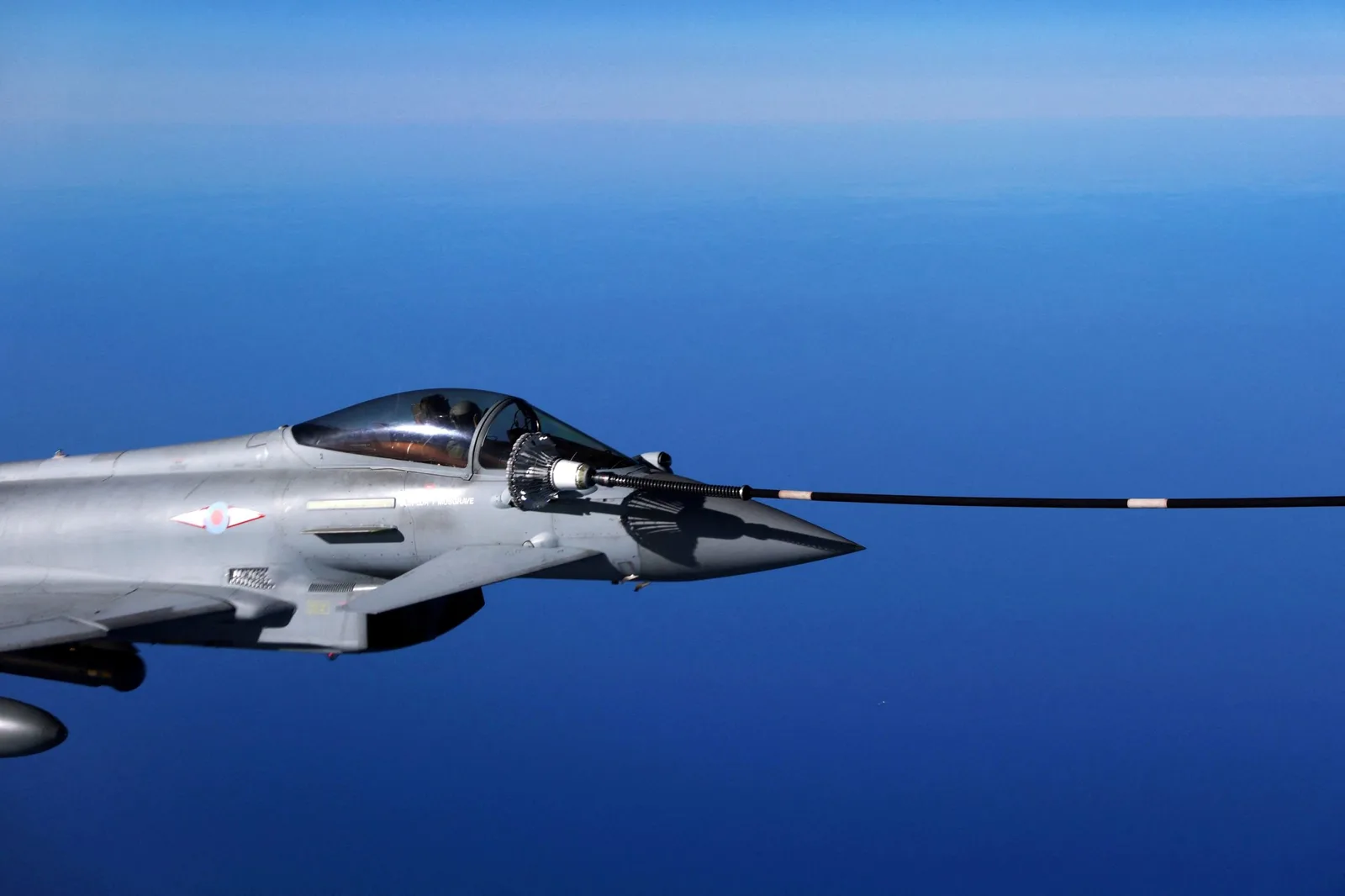 Avion militar în zbor, cu fundal albastru de cer.