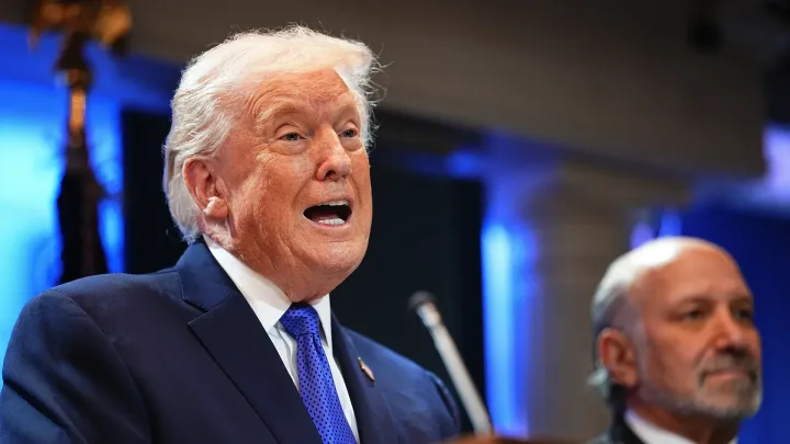 Donald Trump vorbește la o conferință, cu un fundal albastru.