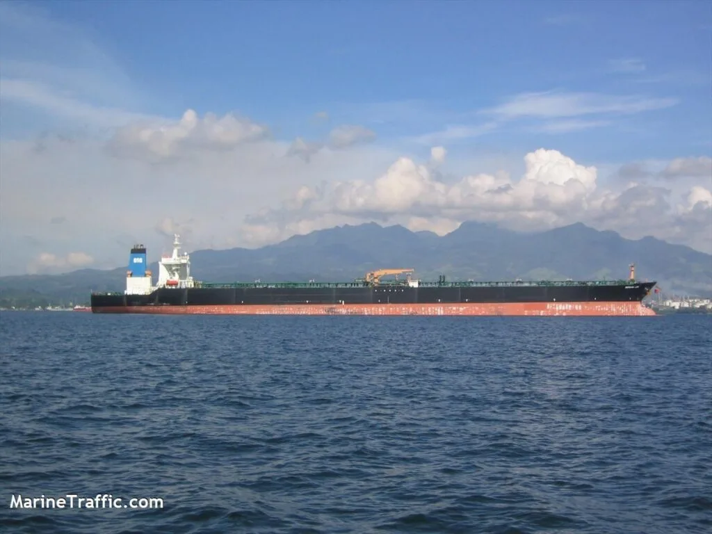 Nava de marfă navigând pe apă, cu munți în fundal.