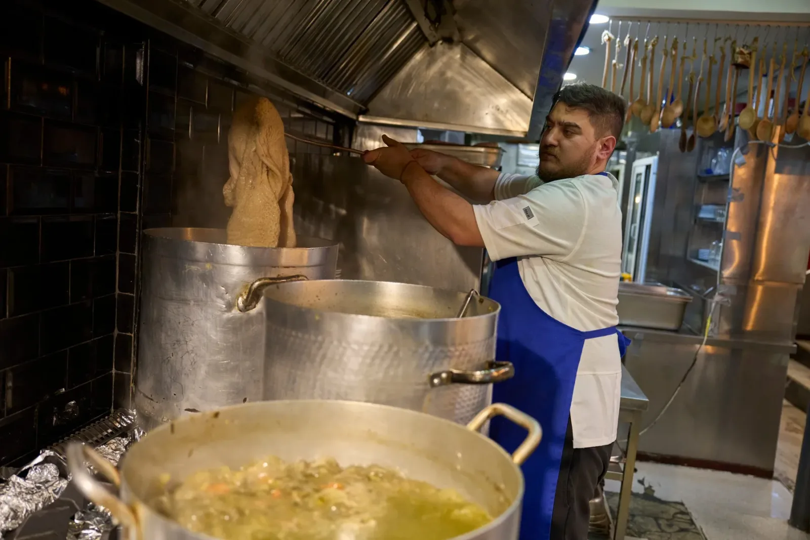 Bucătar pregătind ciorba de burtă într-o bucătărie tradițională.