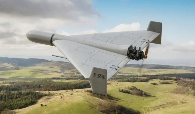 Dronă de tip Geran-2 zburând deasupra unui peisaj verde, cu aripi mari și motor vizibil.