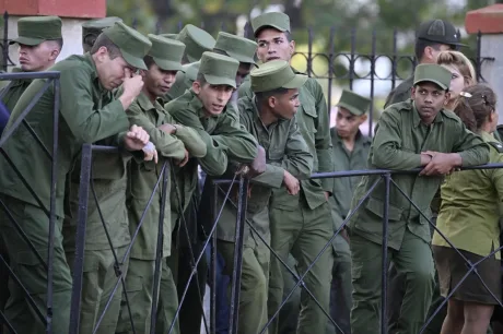 Grup de tineri cubanezi în uniforme militare, discutând la o barieră.
