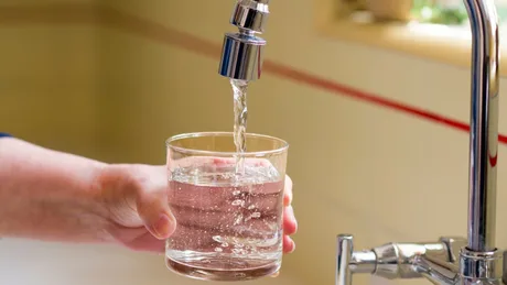 Un robinet care curge apă într-un pahar transparent.