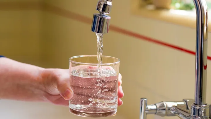 Un robinet care curge apă într-un pahar transparent.