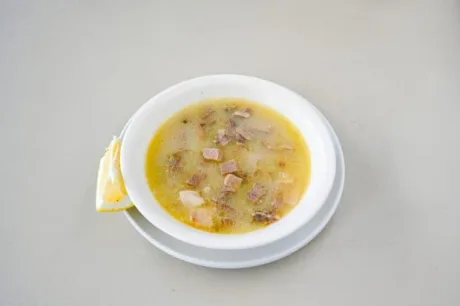 Ciorbă de burtă servită într-un bol alb, cu lămâie alături.