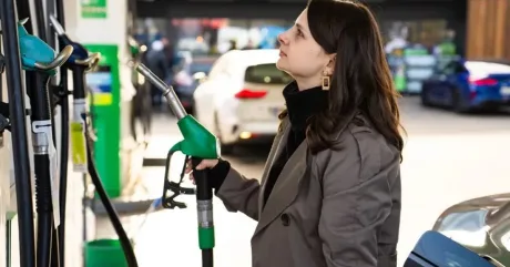 O femeie la o stație de benzină, analizând pompa de combustibil.