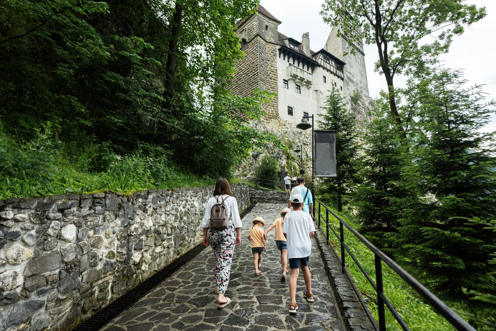 Vizitatori merg pe aleea către Castelul Bran, înconjurat de natură verde.