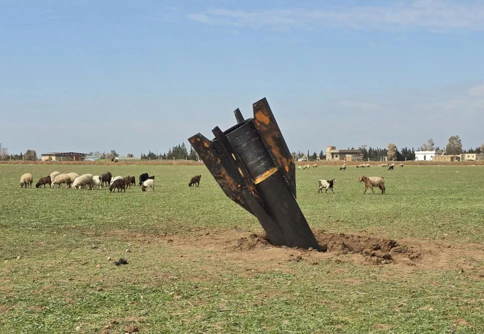 Racheta iraniană înfiptă în pământ, cu oi păscând în apropiere.