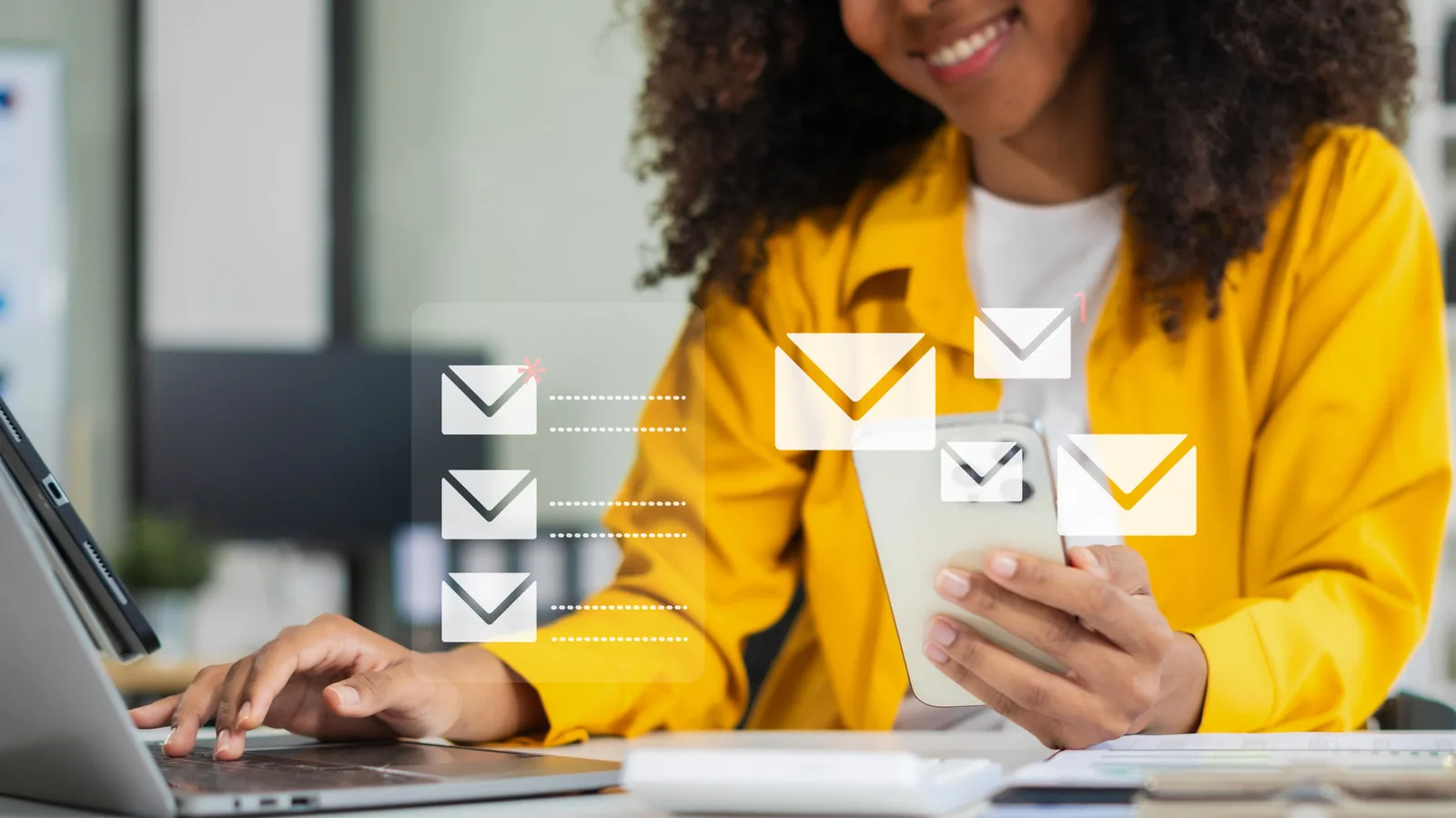 O persoană zâmbitoare verifică emailuri pe telefon și laptop.