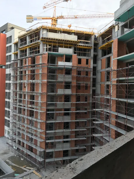 Construcții de locuințe în stadiu avansat, cu schele și utilaje vizibile.