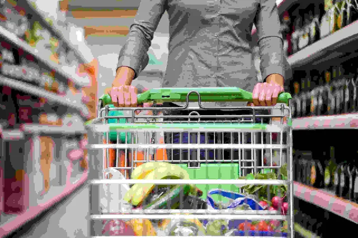 Persoană cu un cărucior de cumpărături plin de alimente în supermarket.