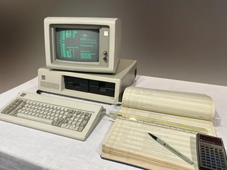 Un computer vechi cu monitor, tastatură și documente tehnice pe masă.
