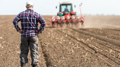Fermier român observând lucrările agricole pe un câmp arat.
