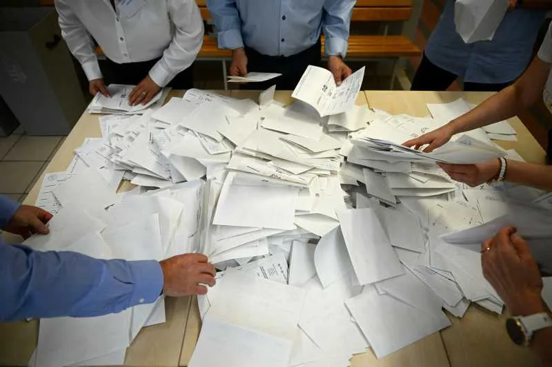 Persoane sortând documente pe o masă, într-un mediu de lucru aglomerat.