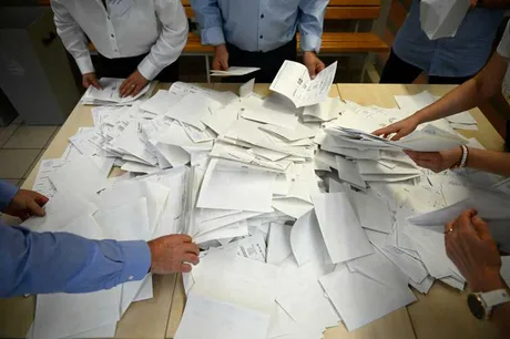 Persoane sortând documente pe o masă, într-un mediu de lucru aglomerat.