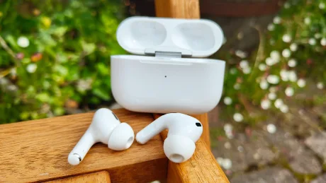 Căști AirPods Pro 3 pe o bancă din lemn, cu flori în fundal.