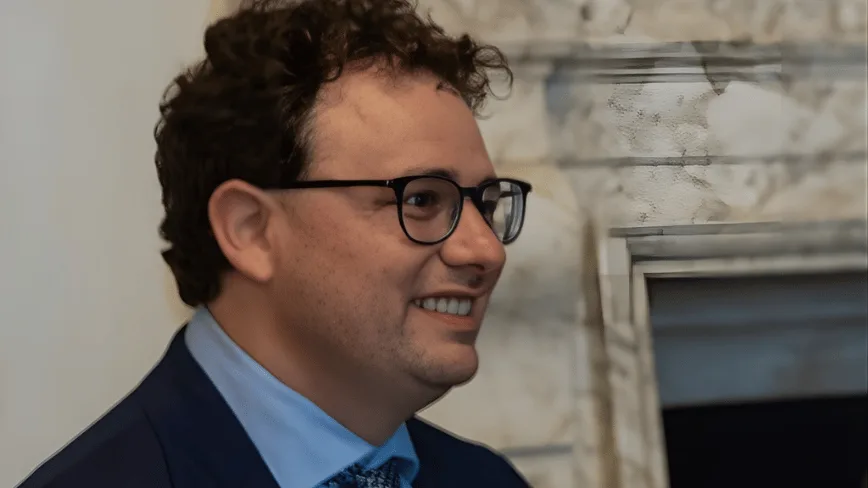 Persoană zâmbitoare într-un mediu elegant, cu detalii arhitecturale în fundal.