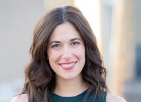 Persoană zâmbitoare cu părul ondulat, în fundal un peisaj urban.