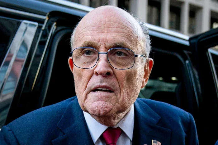 Rudy Giuliani, cu o expresie serioasă, în fața unei mașini.
