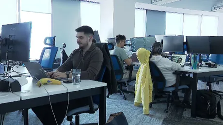 Angajați lucrând într-un birou modern, cu computere și echipamente tehnologice.