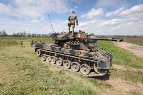Tanc militar pe câmp, soldat în poziție de observație.