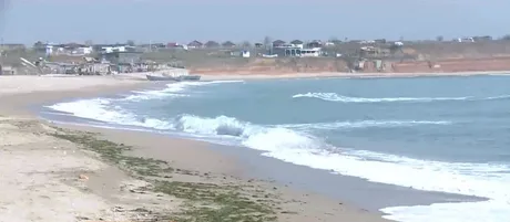 Plaja din Vama Veche, cu valuri și peisaj liniștit, în fundal case de vacanță.