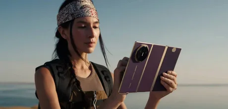 Un utilizator examinează un telefon pliabil cu trei plieri pe fundal natural.