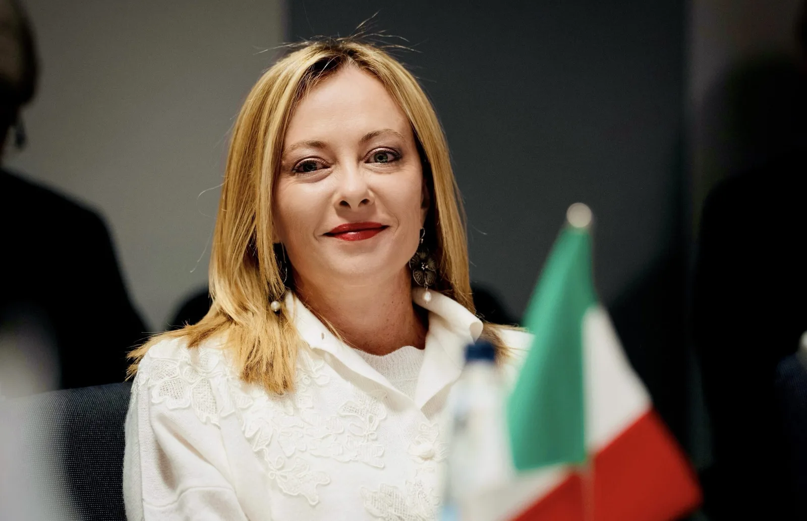 Giorgia Meloni la o întâlnire oficială, zâmbind și purtând o bluză albă.
