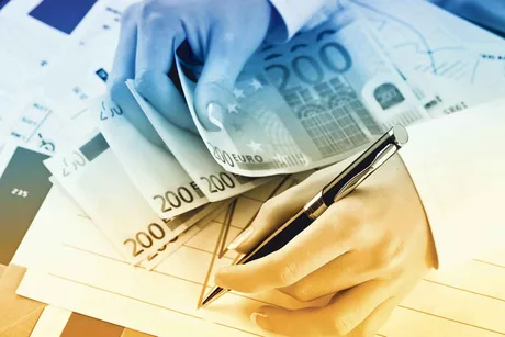Mână care numără bancnote și completează documente financiare.