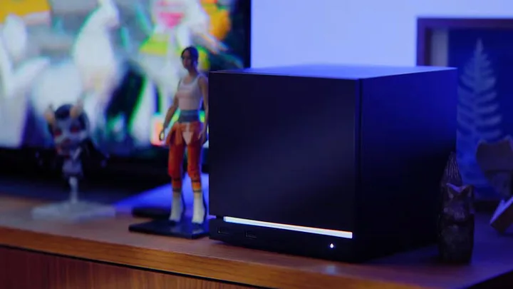 Dispozitiv de jocuri compact, așezat pe un birou, lângă o statuetă.