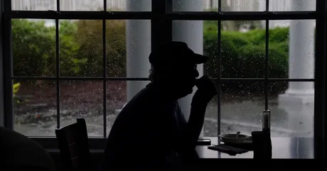 O persoană savurând cafea în fața unei feronerie cu ploaie.