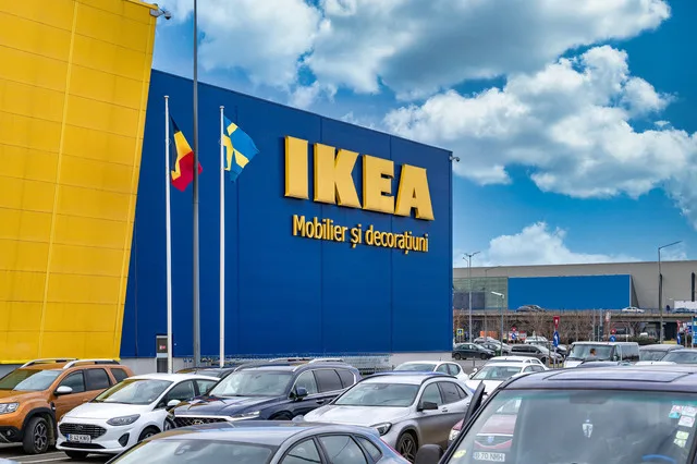 Clădire IKEA cu steaguri, parcări pline și cer senin.