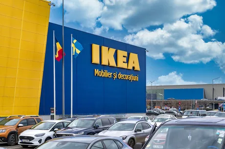 Clădire IKEA cu steaguri, parcări pline și cer senin.