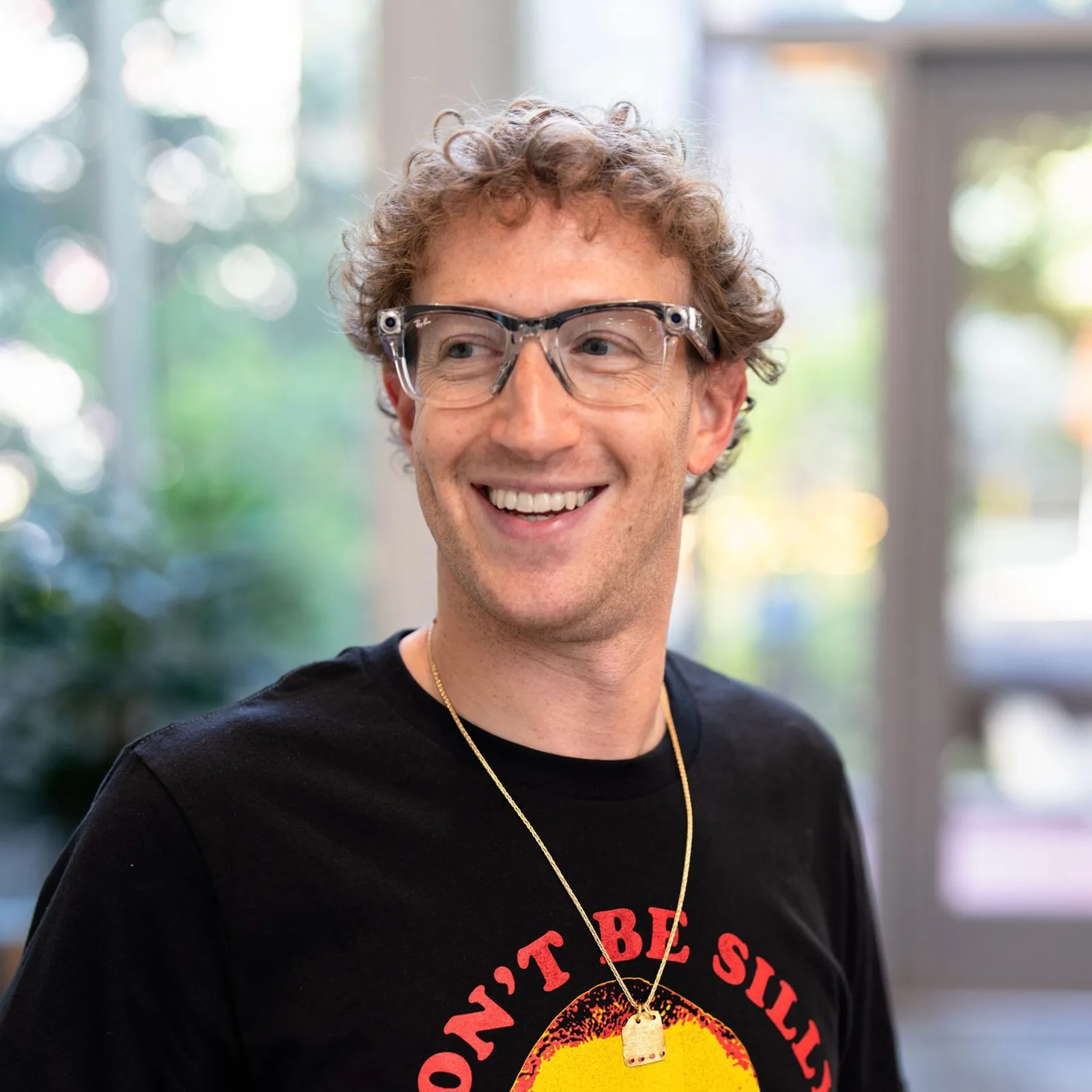 Mark Zuckerberg zâmbind, purtând o bluză neagră și ochelari moderni.